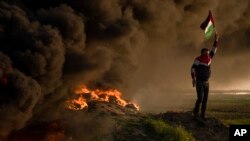 Palestinians burn tires and wave the national flag during a protest against Israeli military raid in the West Bank city of Jenin, along the border fence with Israel, in east of Gaza City Jan. 26, 2023.